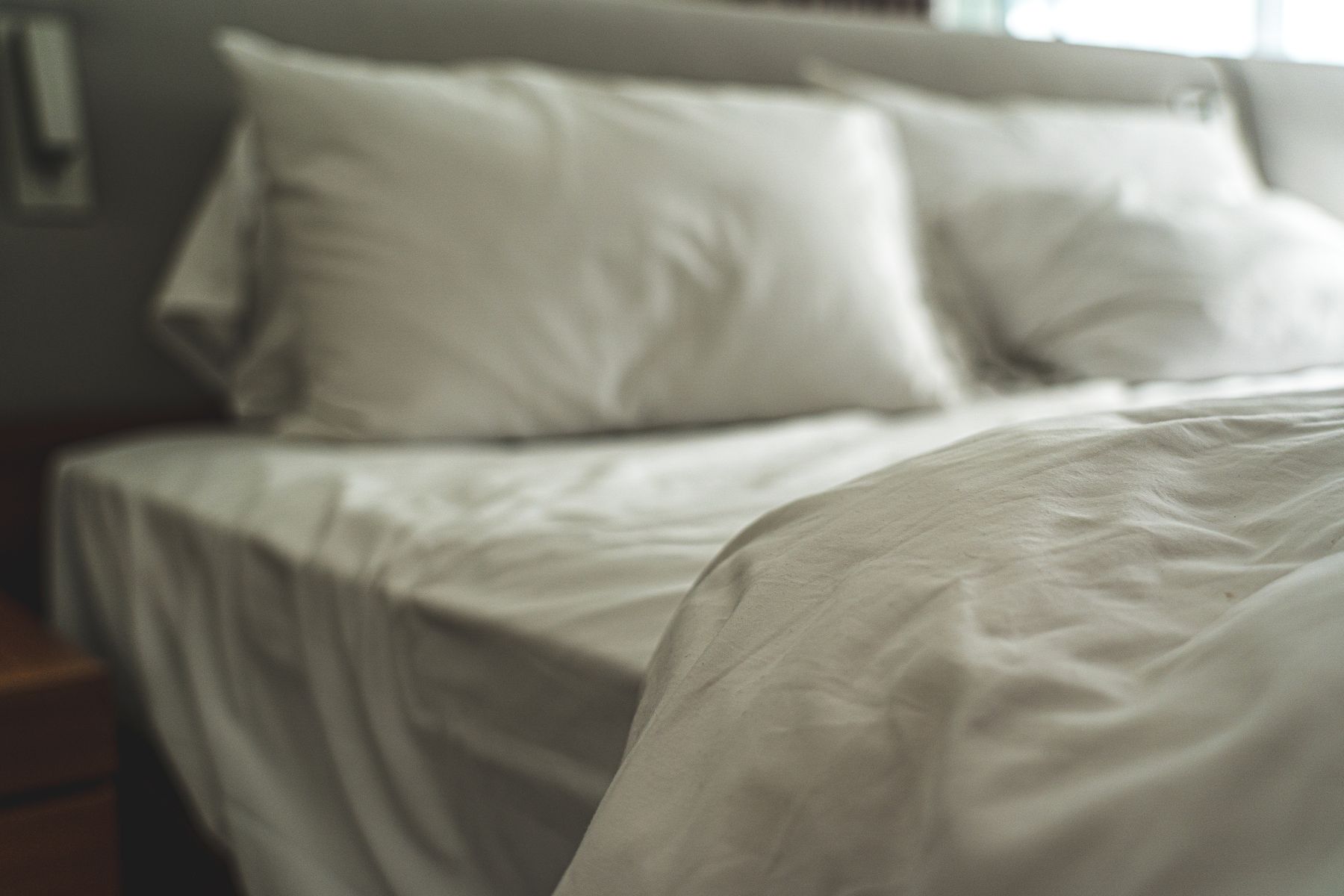 Freshly made bed with white pillows and sheets in soft morning light