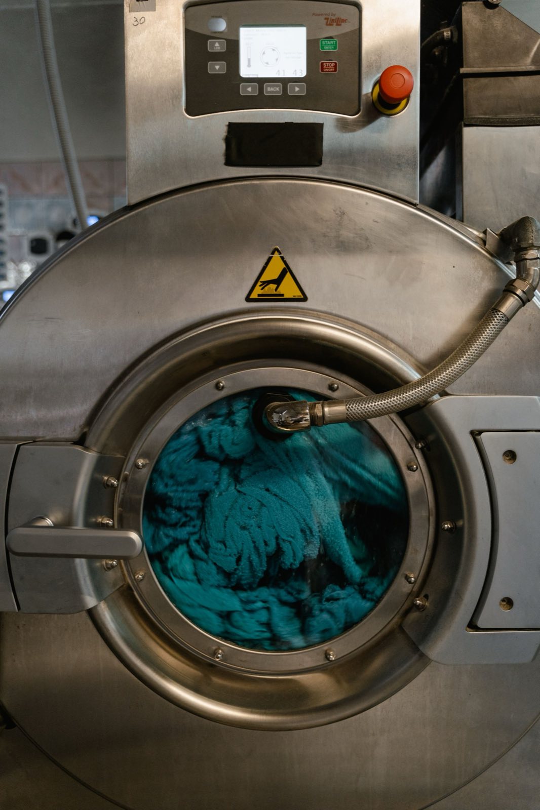 Close-up of an industrial washer-extractor drum loaded with teal linen, stainless steel door open