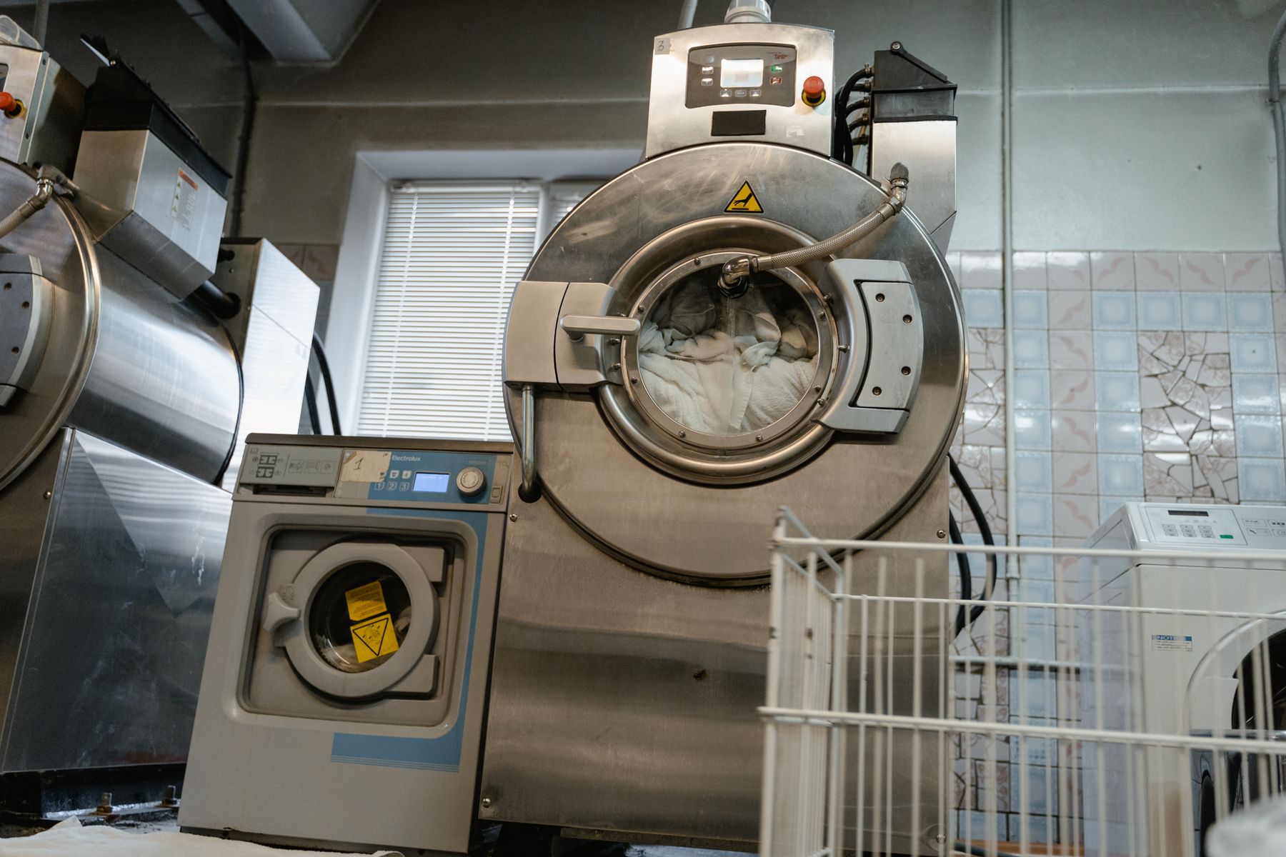 Industrial washer-extractors in an operating laundry room, with a linen basket in the foreground