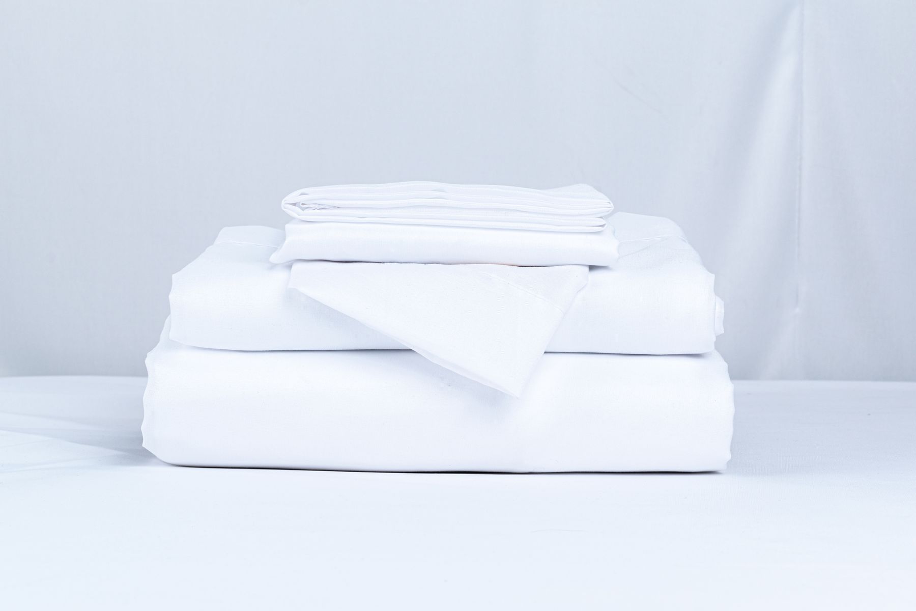 Stack of folded white bed linen on a white table against a plain backdrop