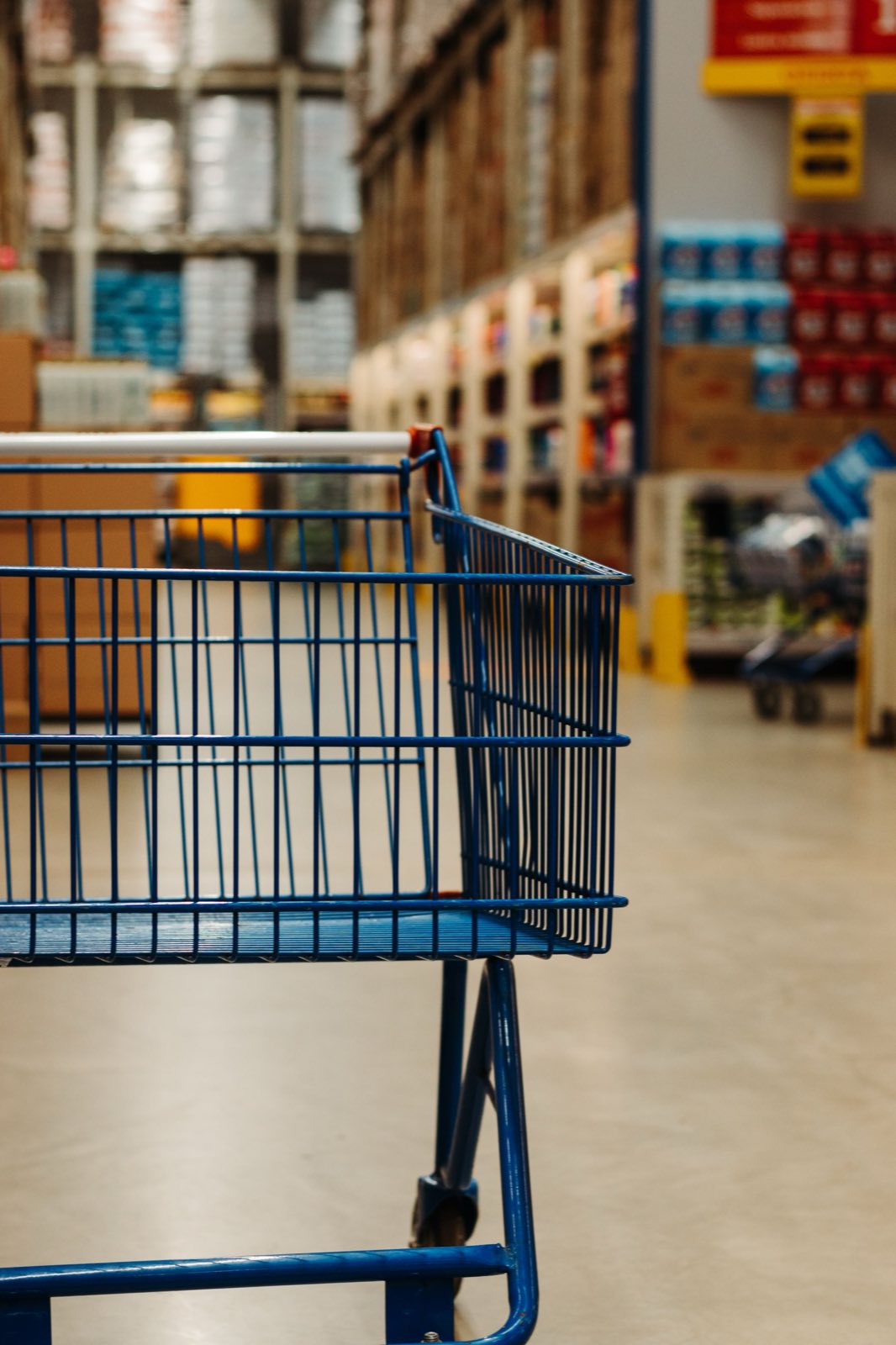 Blue wire shopping cart in the foreground of a large store aisle, shelving blurred behind