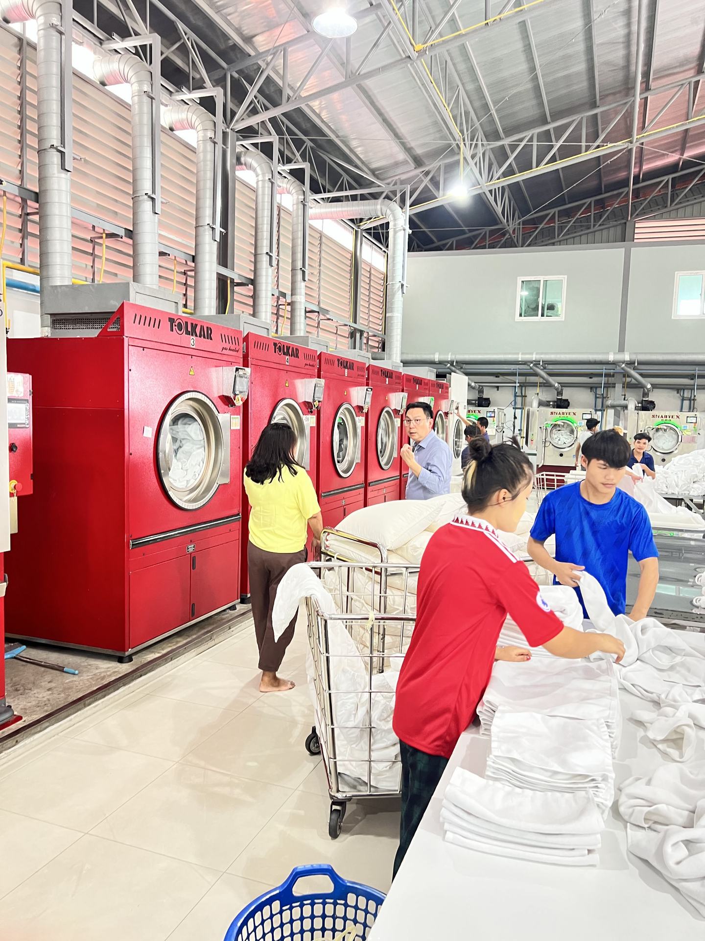 PEO team on the industrial laundry plant floor beside the red washer-extractor line